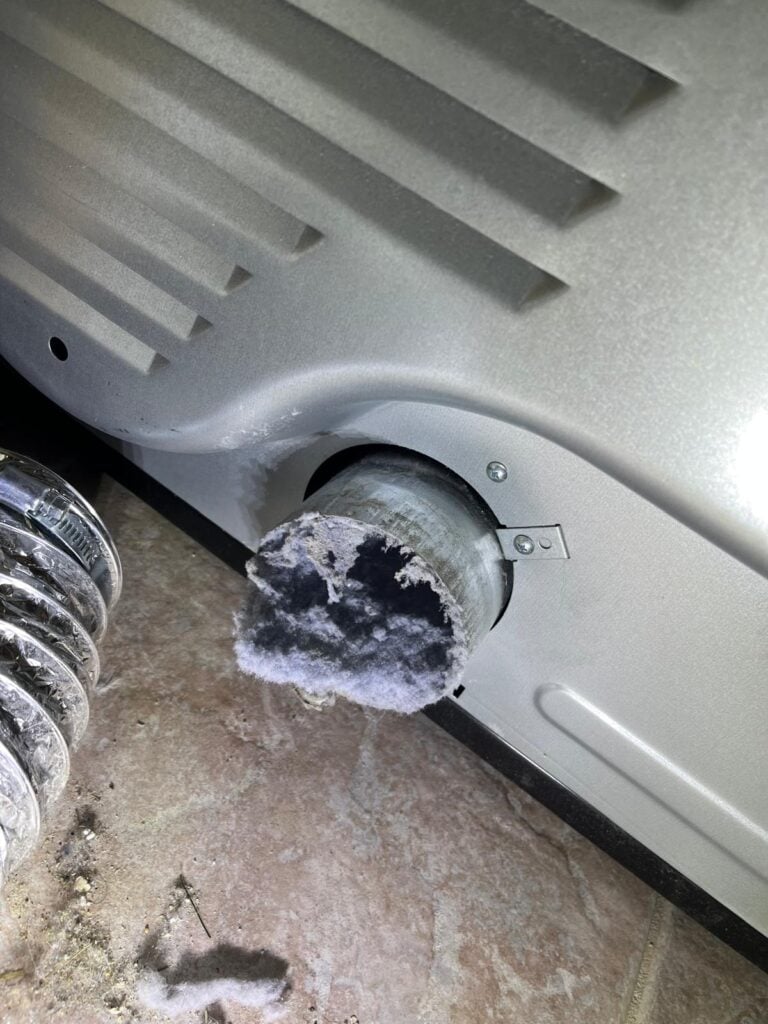Dryer pulled out from wall showing a solid lint plug blocking the back exhaust connection — extreme fire risk before SunDuct cleaning