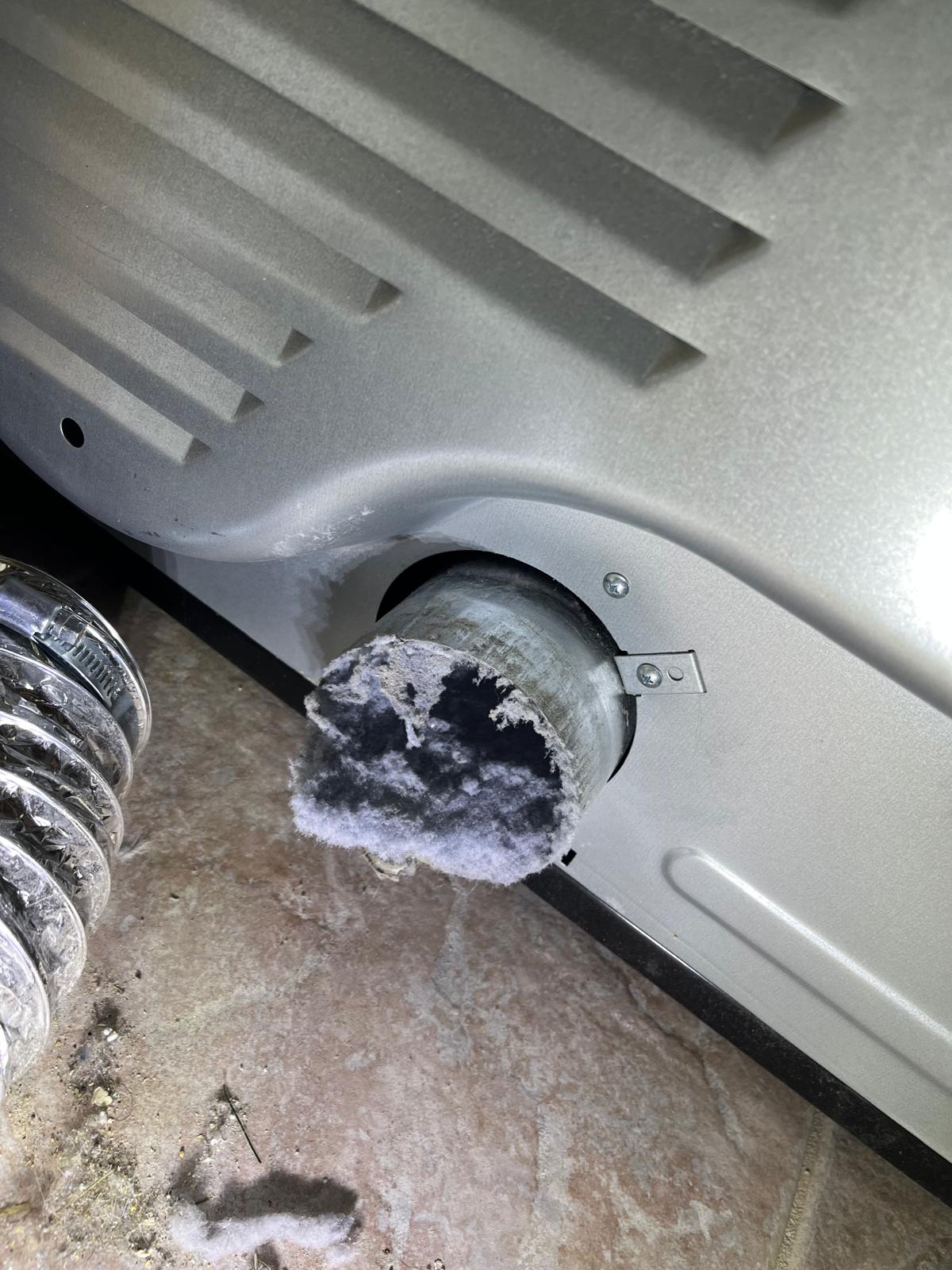 Dryer pulled out from wall showing a solid lint plug blocking the back exhaust connection — extreme fire risk before SunDuct cleaning