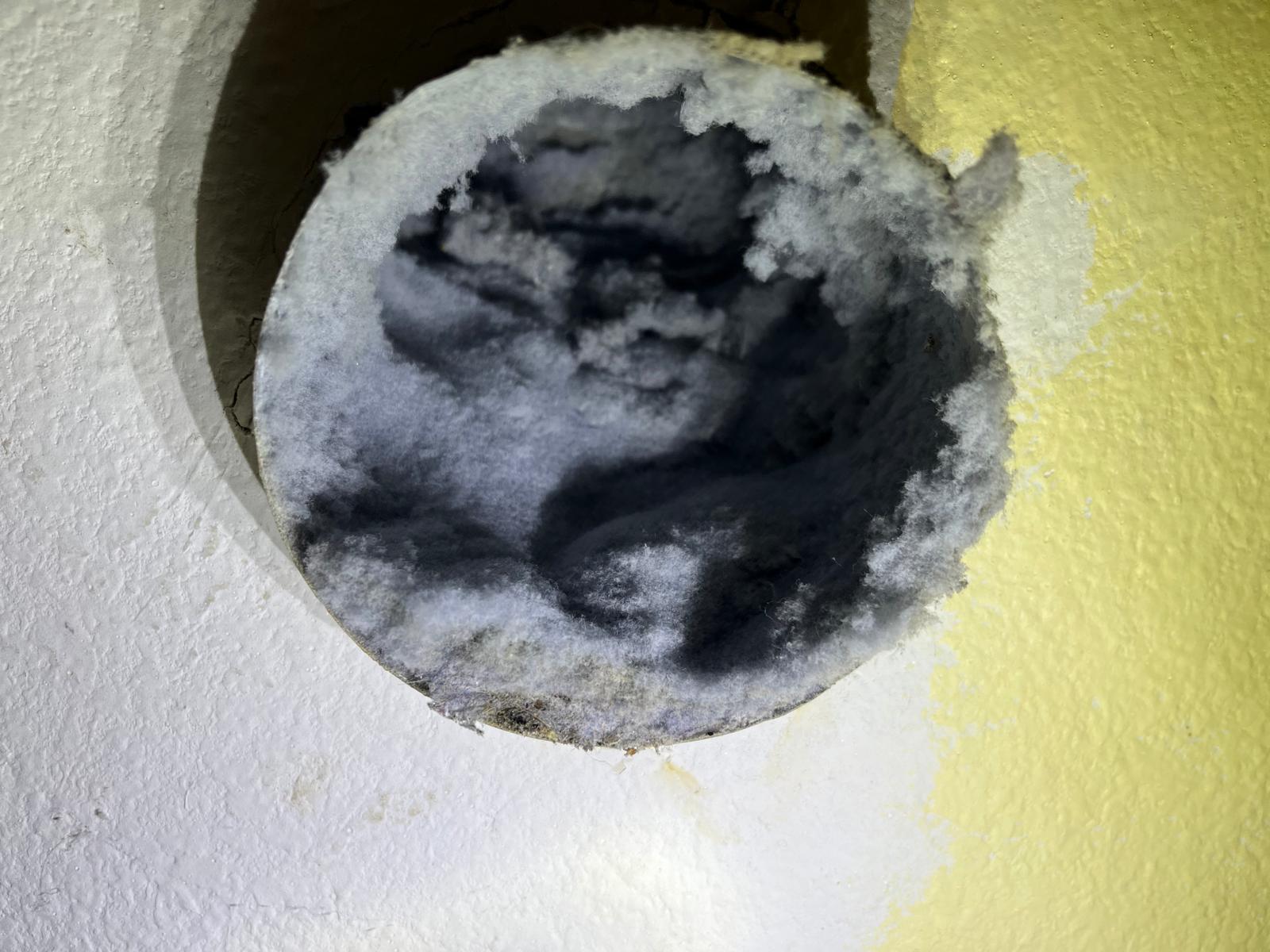Wall dryer vent opening completely blocked with thick lint mat before SunDuct cleaning service in Florida