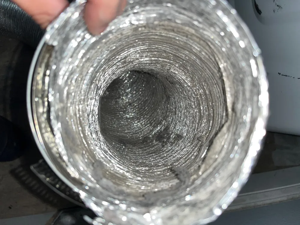Technician inspecting a lint coated dryer duct during a dryer vent cleaning visit in Florida